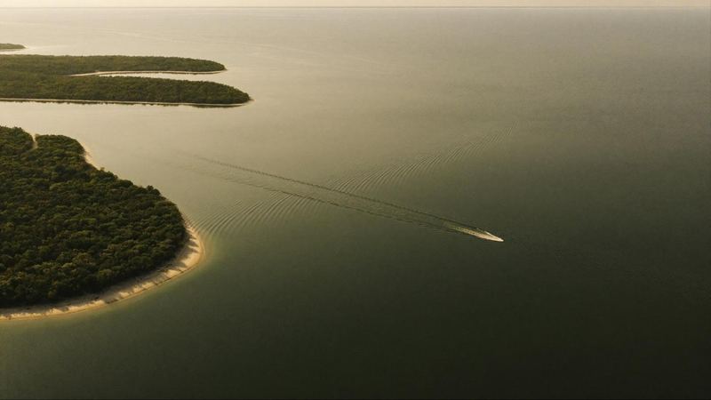 Aerial view of the Intracoastal Waterway in South Florida at first light, a single boat drawing a wake across still green water.