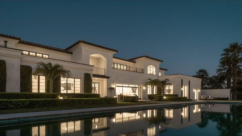 A Mediterranean residence at dusk, warmly lit from within, mirrored in a long reflecting pool.