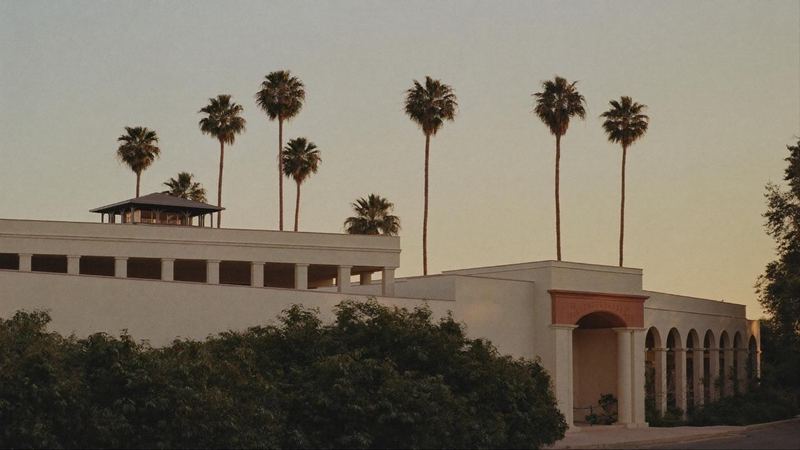 A cream Mediterranean revival building with an arcaded loggia, framed by tall palms against a warm dusk sky.